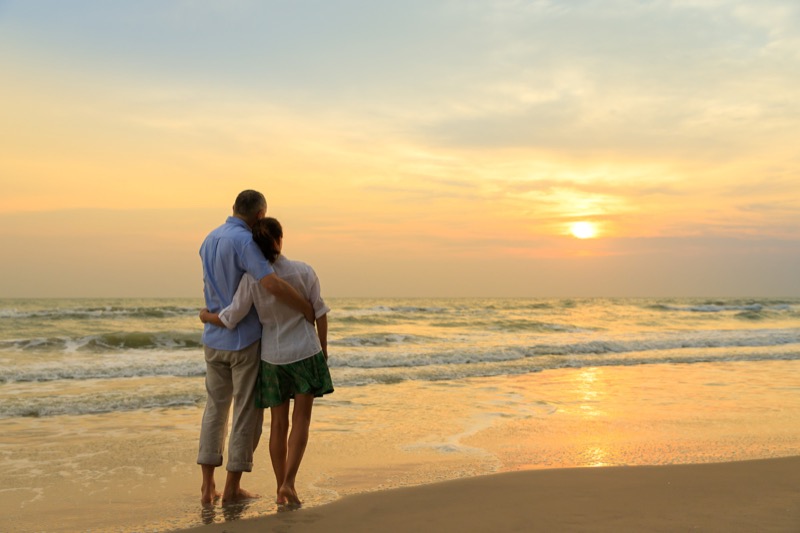 Casal abraçado observando o pôr do sol na praia